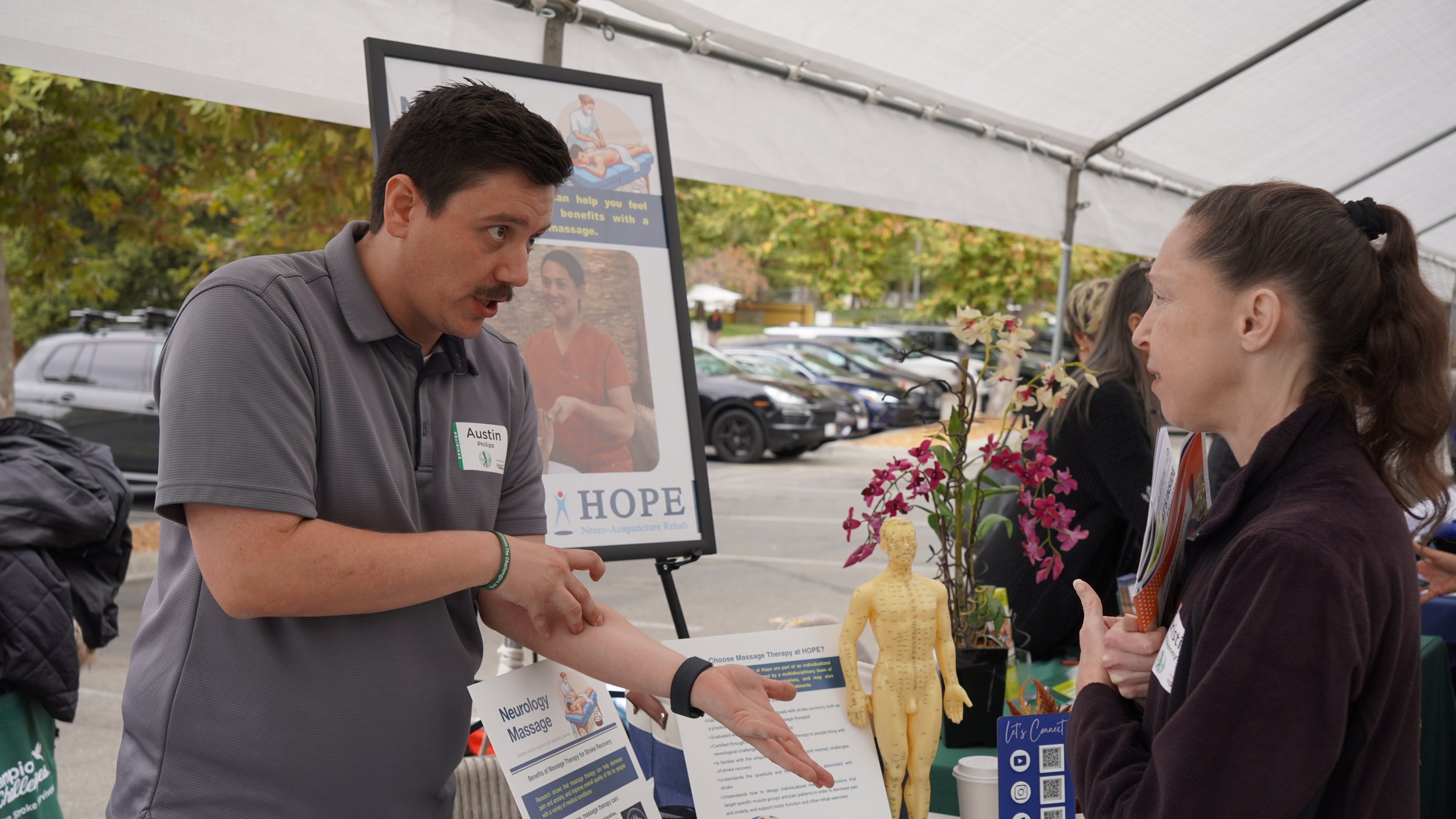 HOPE Clinic staff member presenting acupuncture information to visitors at outdoor community event