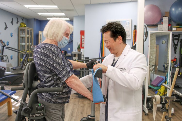 Dr. Lu helping patient with resistance band exercises using standing frame in rehab gym