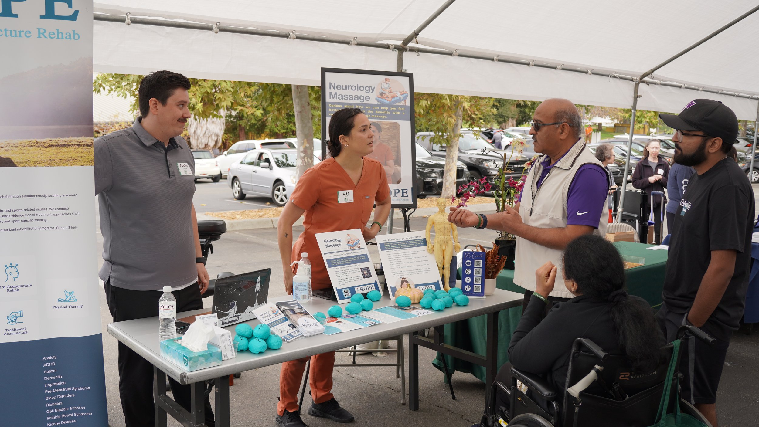 HOPE Clinic staff members and therapist talking with visitors at outdoor community event booth