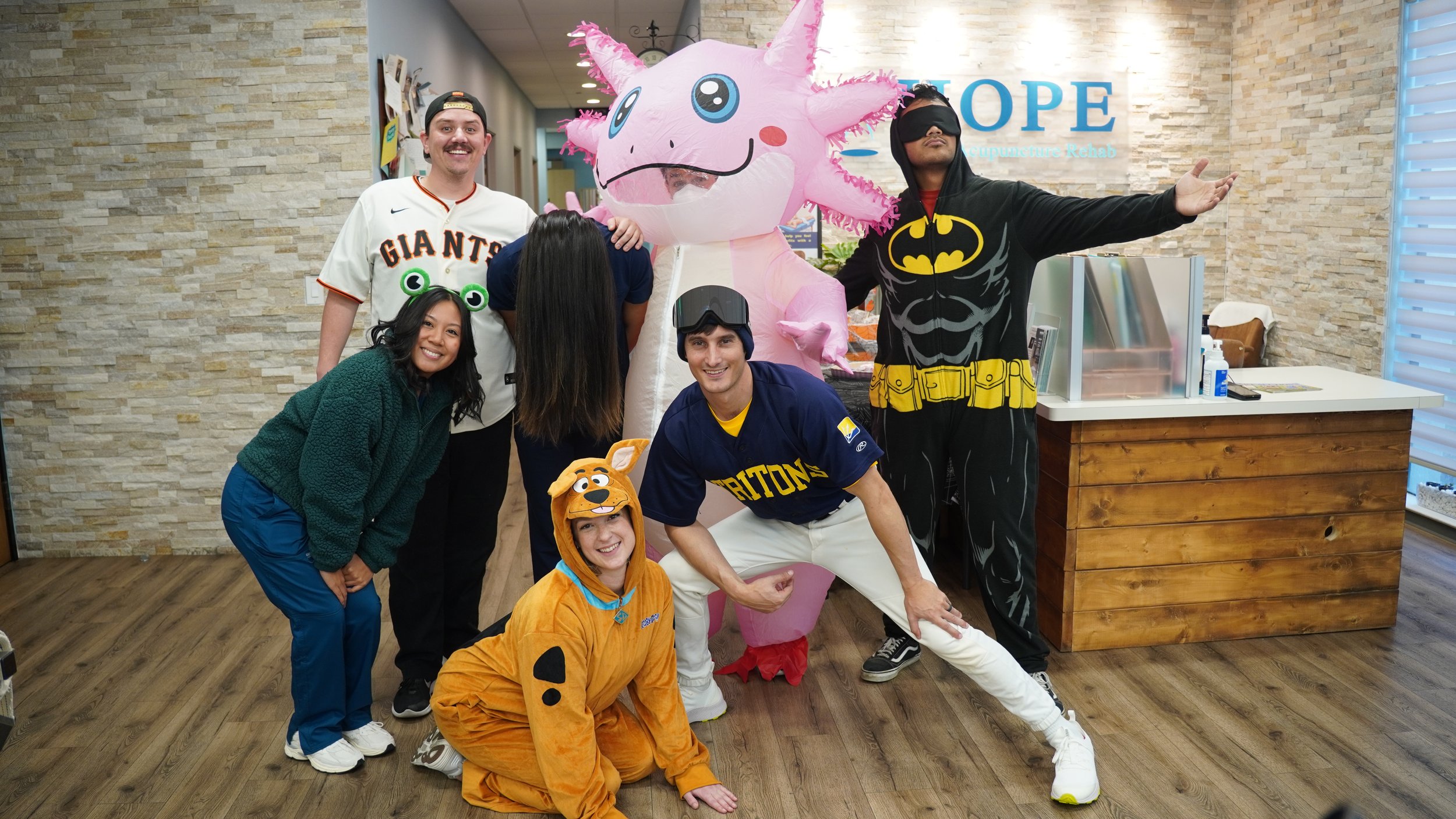 HOPE Clinic team in Halloween costumes posing in lobby with axolotl and Batman inflatable suits
