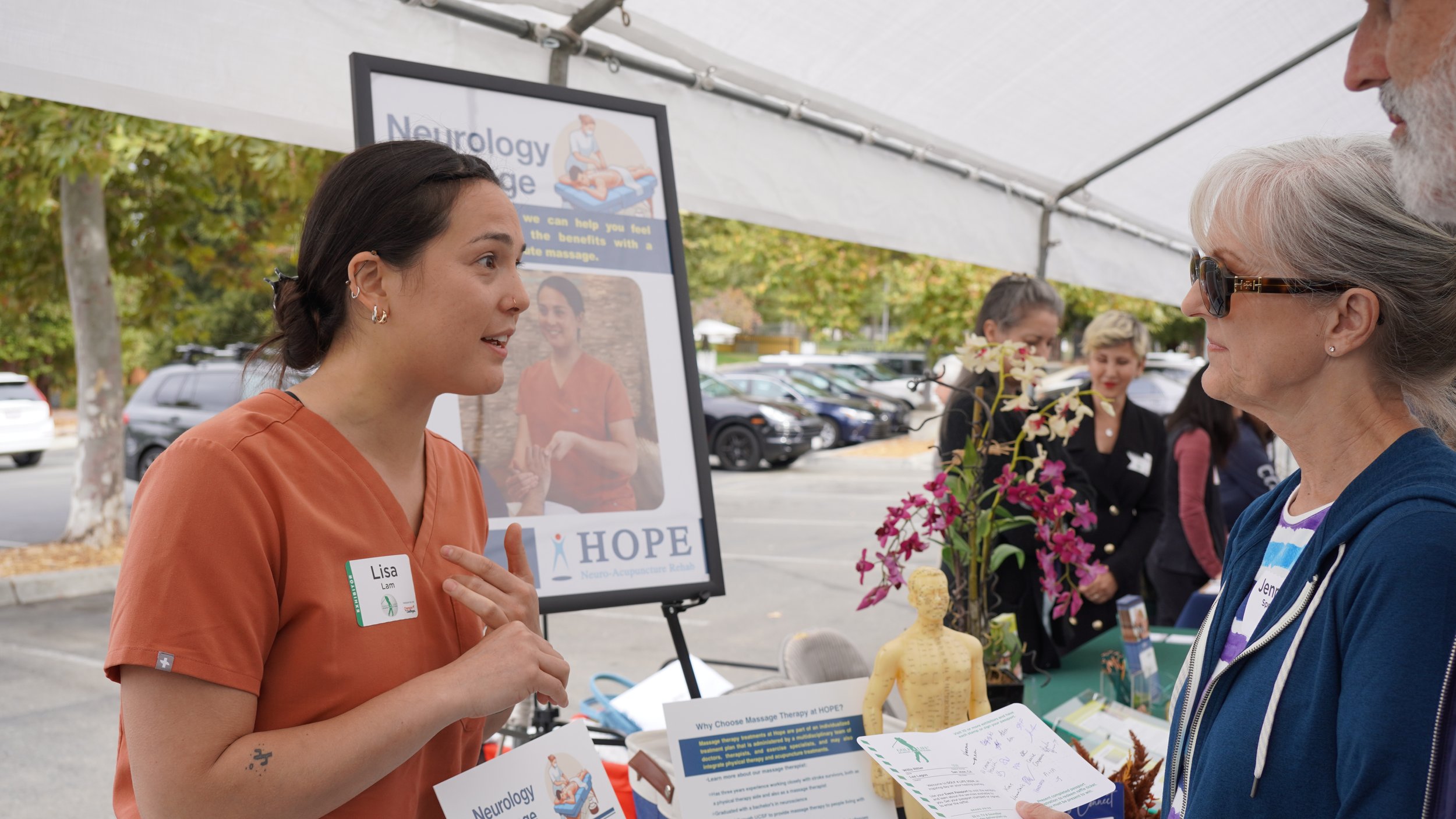HOPE massage therapist explaining neurology massage services to attendee at community event