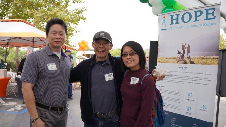 Dr. Lu with patient and spouse posing at HOPE Clinic community event banner