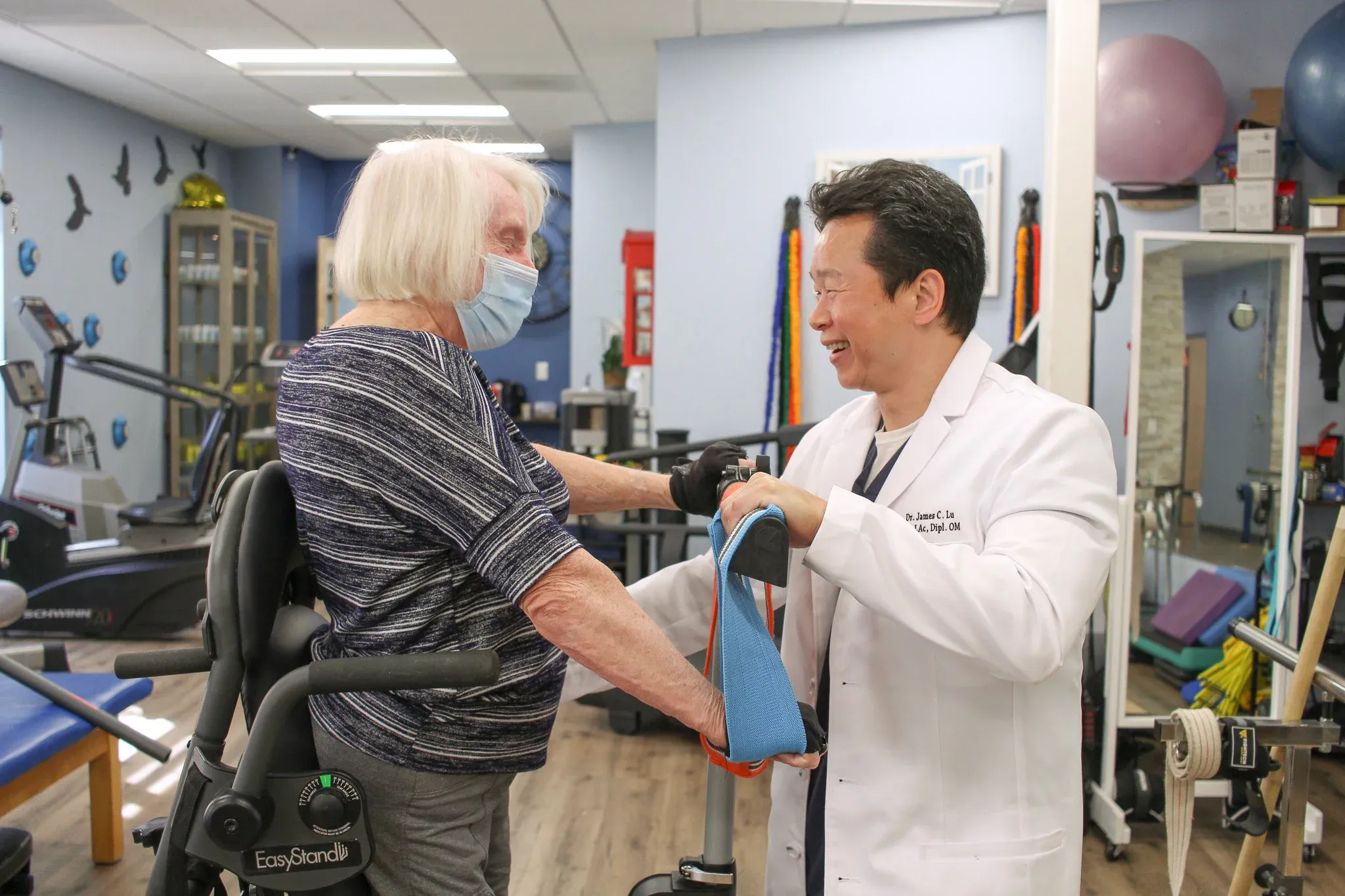 A healthcare professional assisting an elderly woman with a mobility aid in a rehabilitation gym